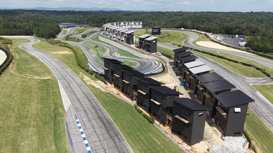 Aerial view of the Circuit Villas clad in dark gunmetal siding, the car circuit running along the near side and the kart circuit behind, with the North Georgia foothills on the horizon