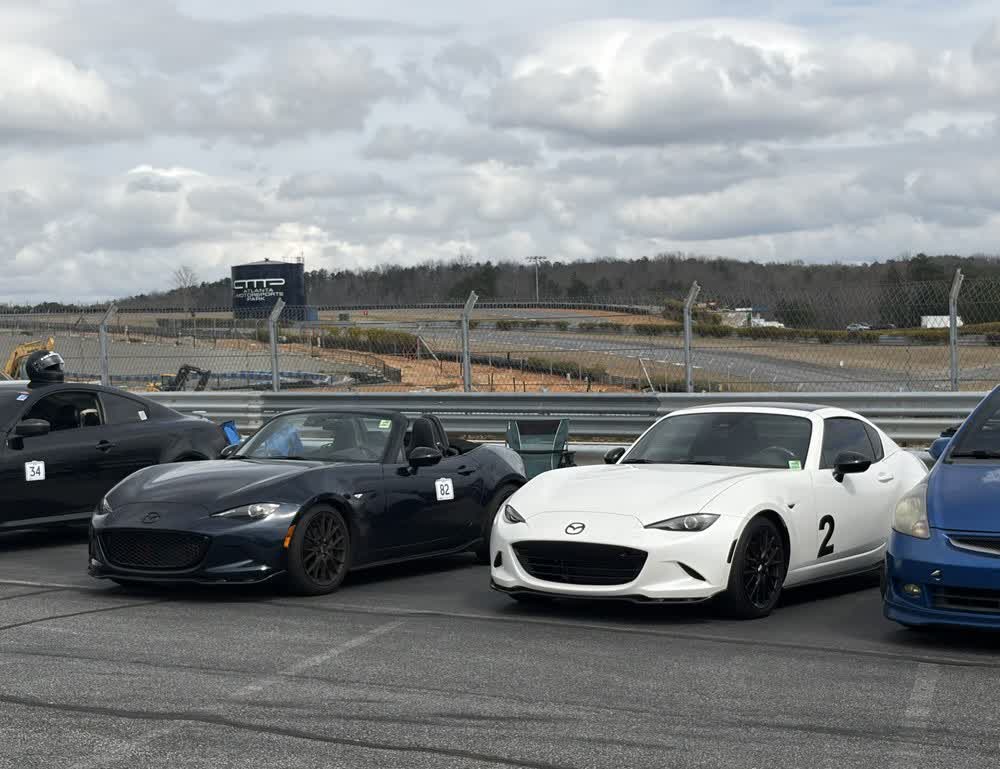 Four cars parked in the paddock at Atlanta Motorsports Park, numbers taped to their doors, the circuit behind