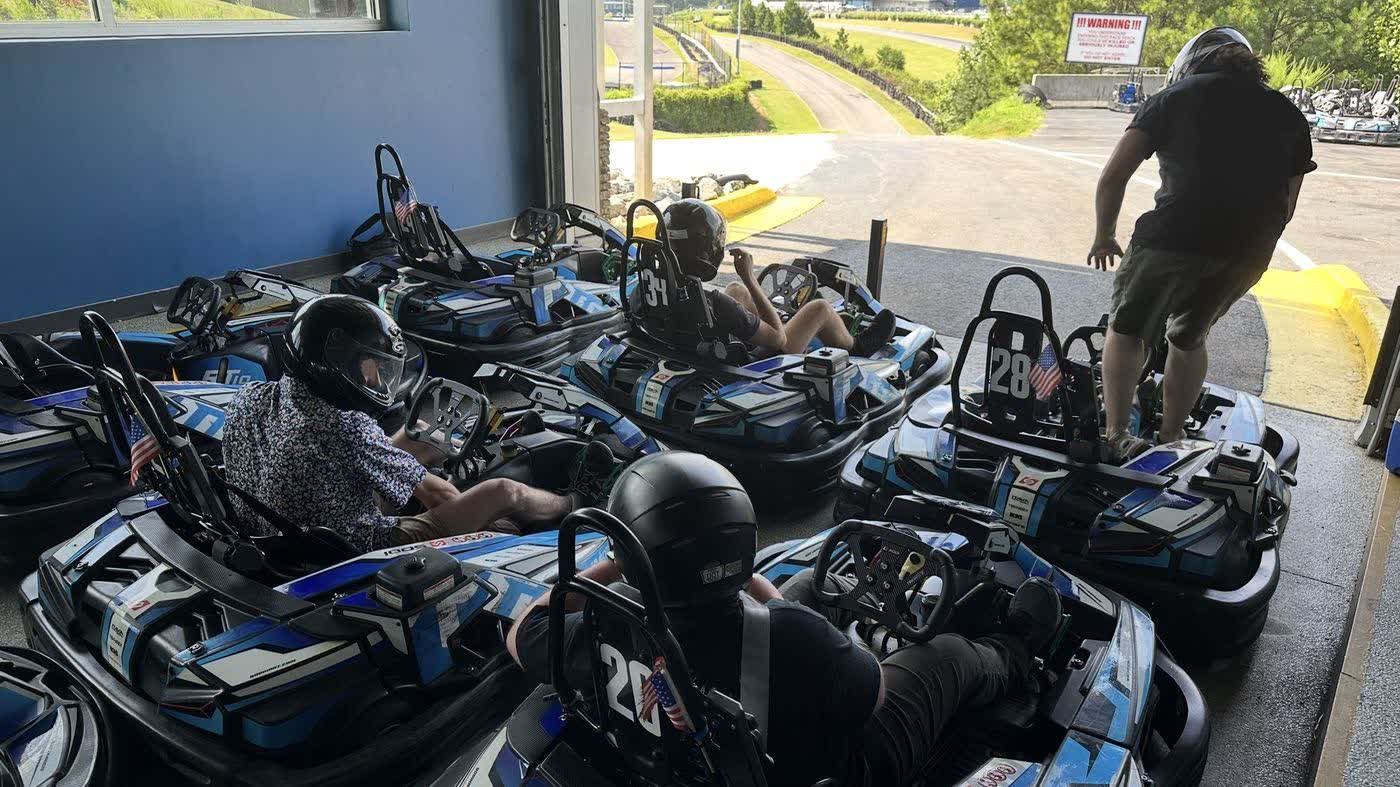 Karts lined up in the staging lane at AMP Kart Racing, drivers belted in, the door open onto the circuit